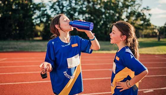 Two girls on a track field drinking water after training