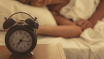 一个女人躺在床上看着闹钟.